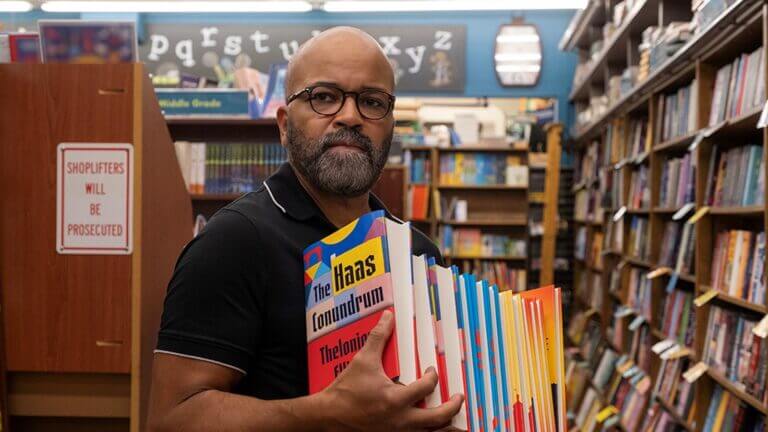 A man in a book store holds a stack of books.
