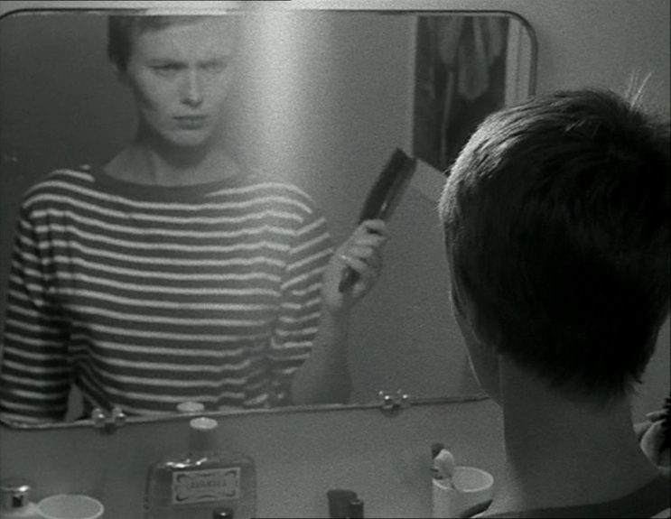 Patricia makes a face into her bathroom mirror while holding a comb
