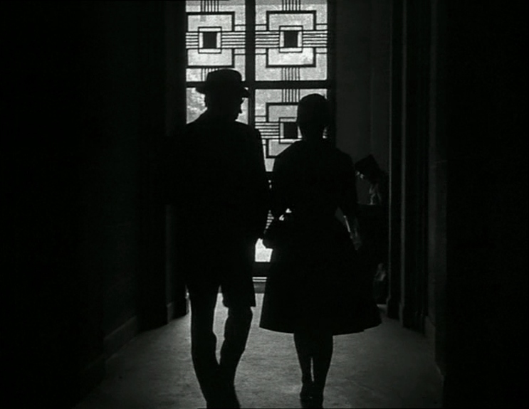 The silhouettes of Michel and Patricia walk down a hallway