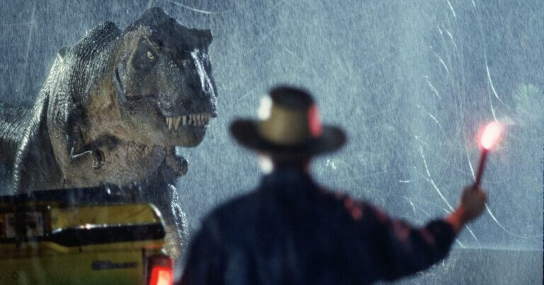 A man holds a flare and stares down a Tyrannosaurus rex