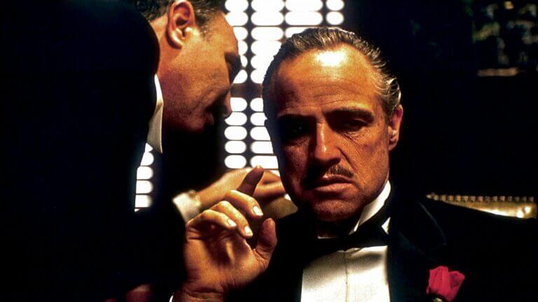 Tom Hagen leans over to whisper in Vito Corleone's ear