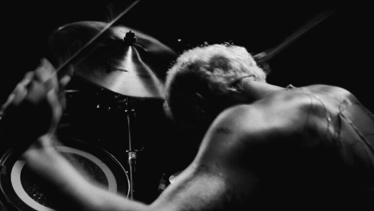 A shirtless drummer plays heavy metal