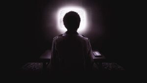 A teenager sits in the dark in front of a glowing TV screen