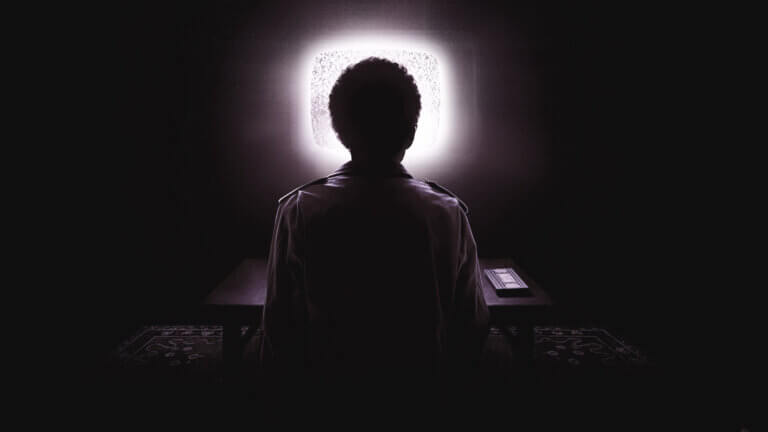 A teenager sits in the dark in front of a glowing TV screen
