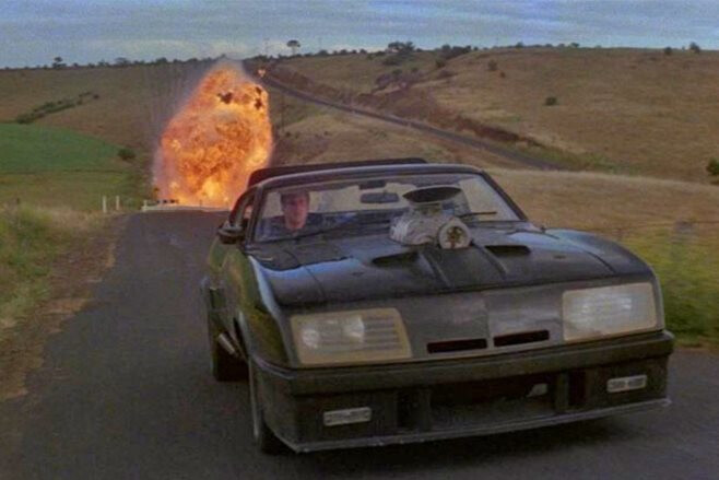 Mad Max drives away from an explosion