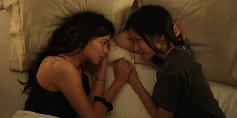 Lucy and Jane hold hands in bed.
