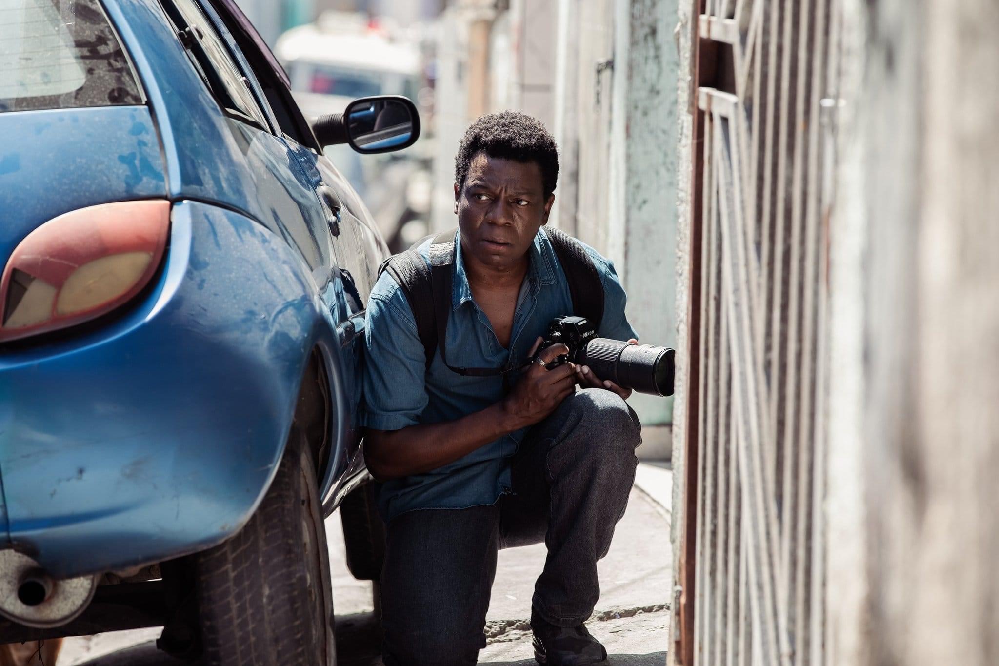 Buscapé crouches behind a car, waiting to take a photo