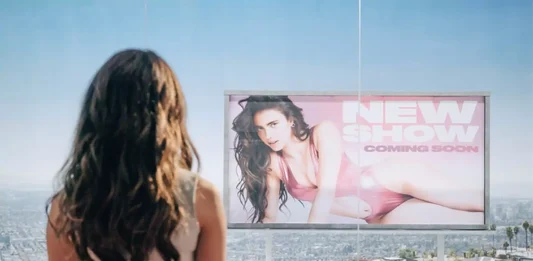 Sue looks out the window at a billboard of herself.