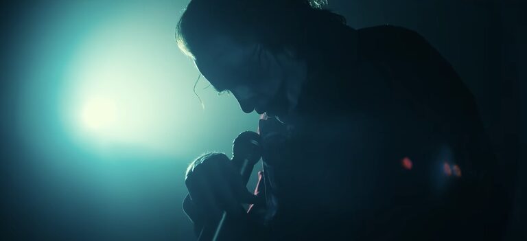 Joker holds a microphone, sadly, as he sings on stage