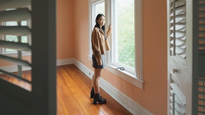 A girl stands in an empty room and looks out the window.