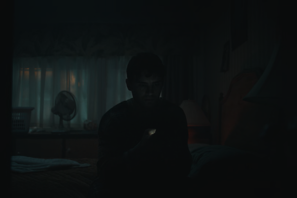 Bear sitting in the dark in his room, holding his phone